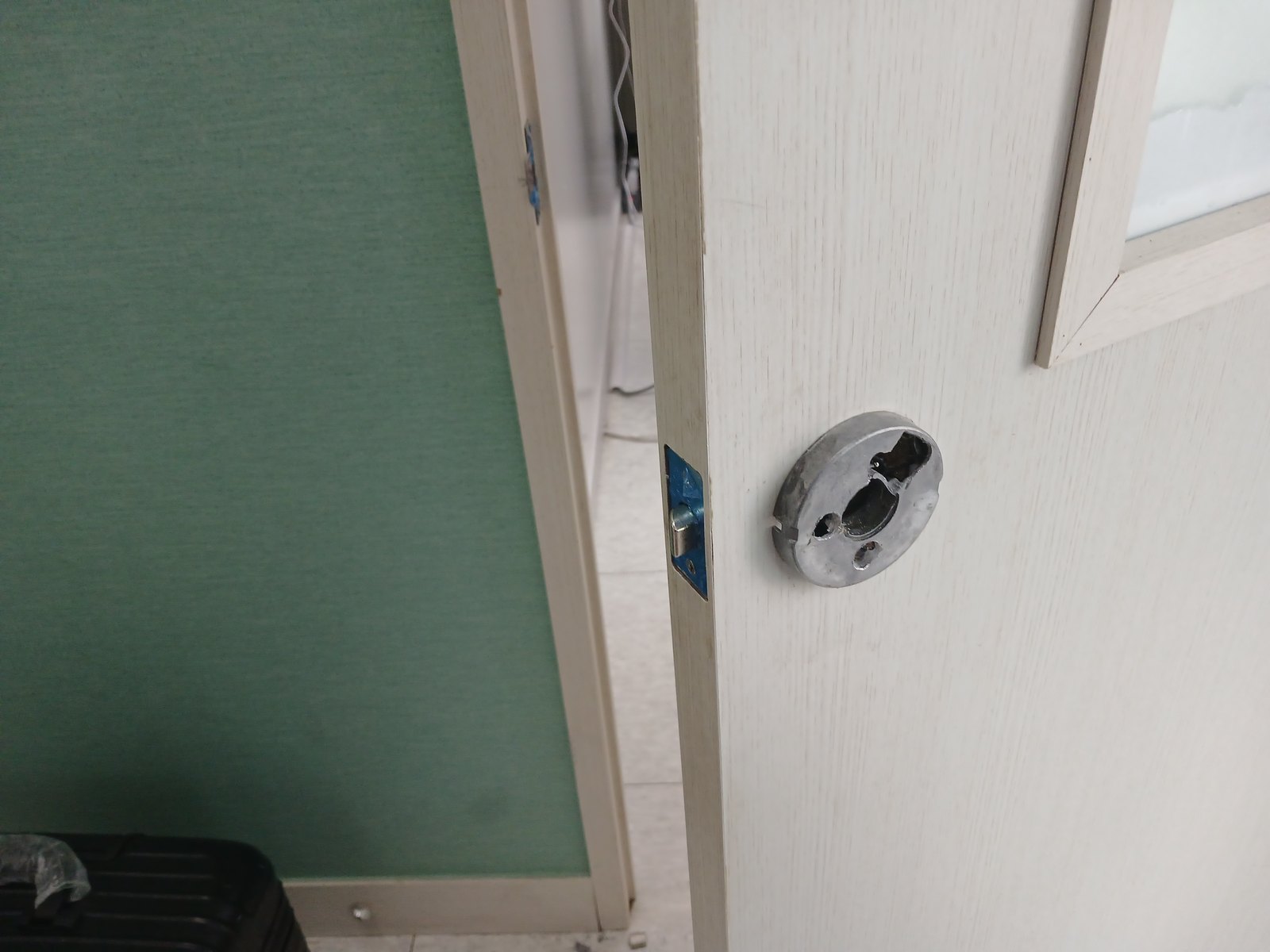 일산서구 탄현1동 출장 — 손잡이를 떼어 낸 밝은 나뭇결 문의 둥근 은색 받침과 파란 필름이 붙은 옆면 걸쇠